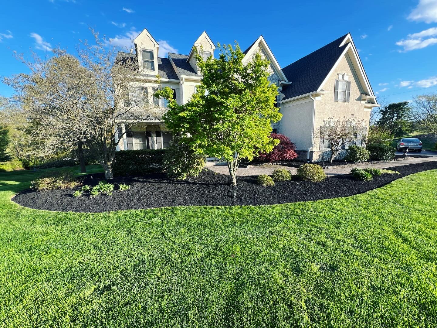 Freshly mulched landscape beds around a stone home with lush green lawn