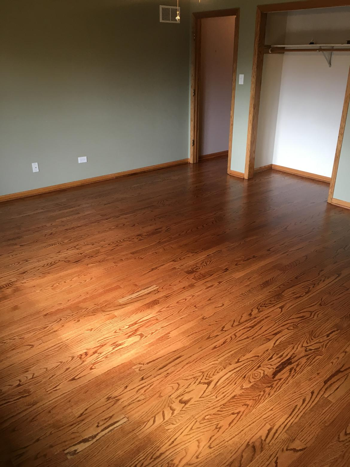 Freshly installed red oak hardwood flooring in a bedroom with sage green walls
