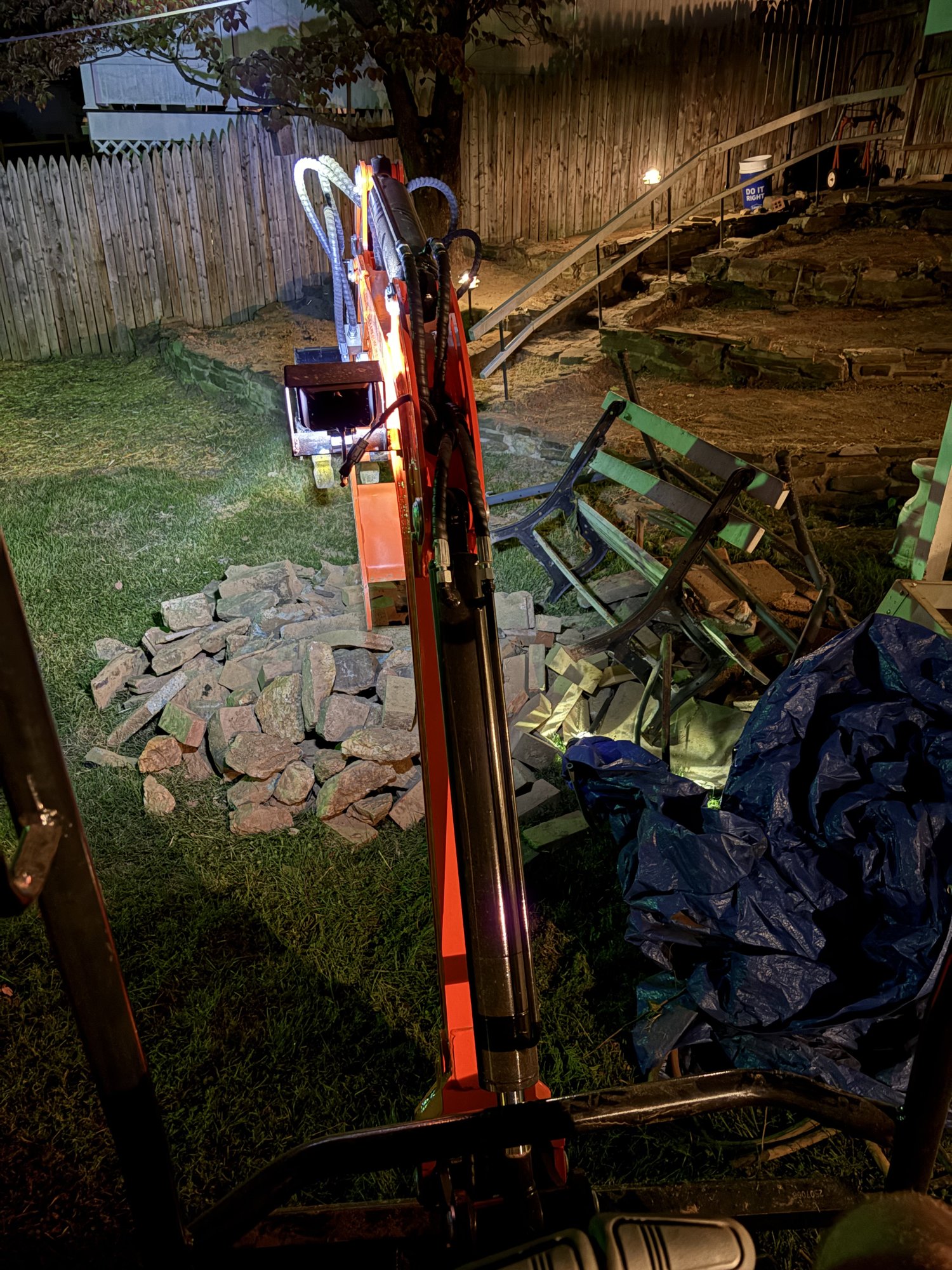 Larson Landscape mini excavator on a backyard demo job with stacked stone rubble and debris ready for haul-away