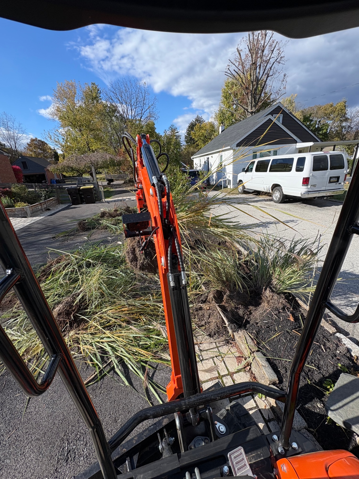 Mini excavator removing overgrown ornamental grasses from a landscape bed