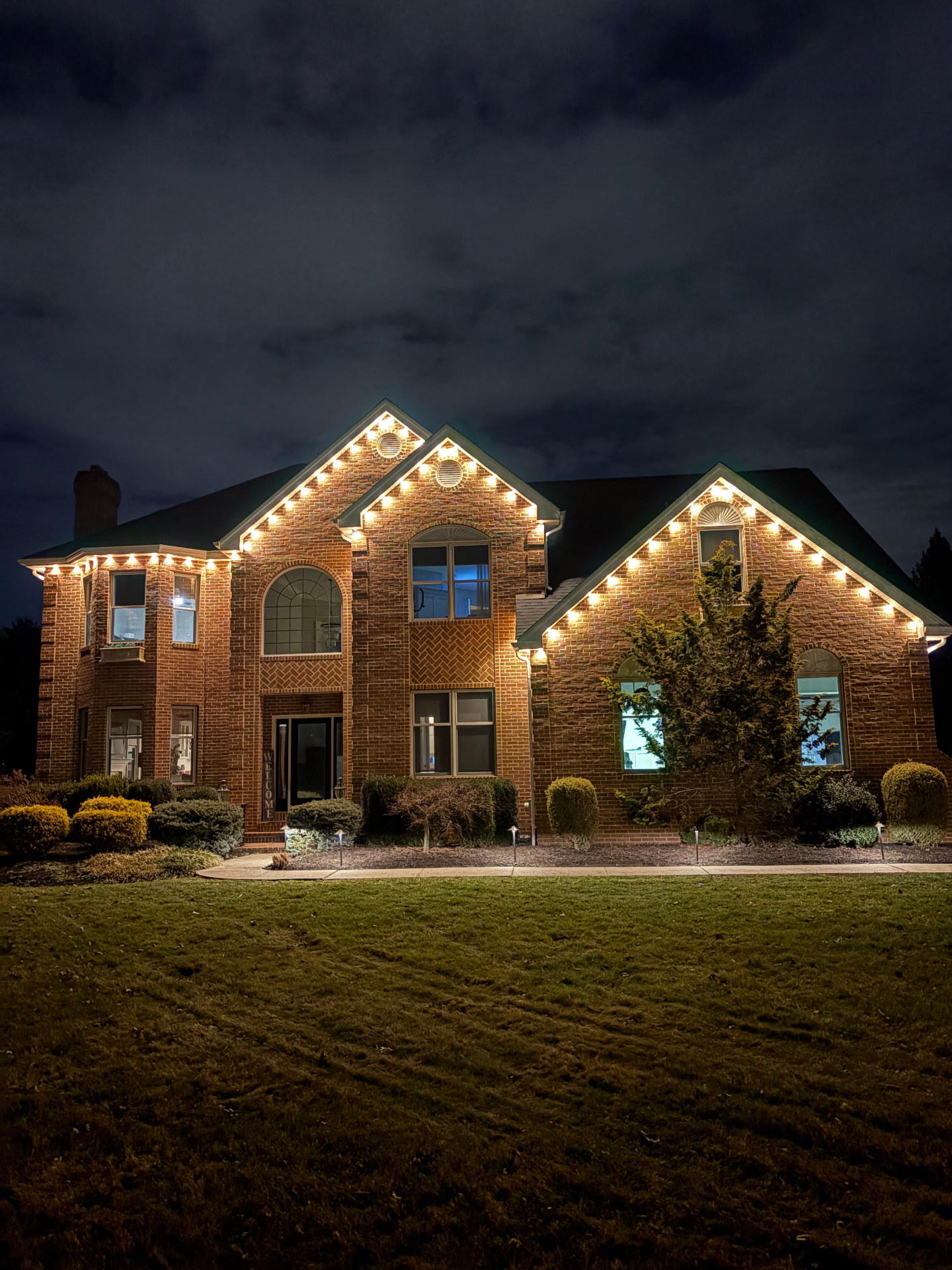 Brick home at night with warm white roofline lighting and landscape path lights